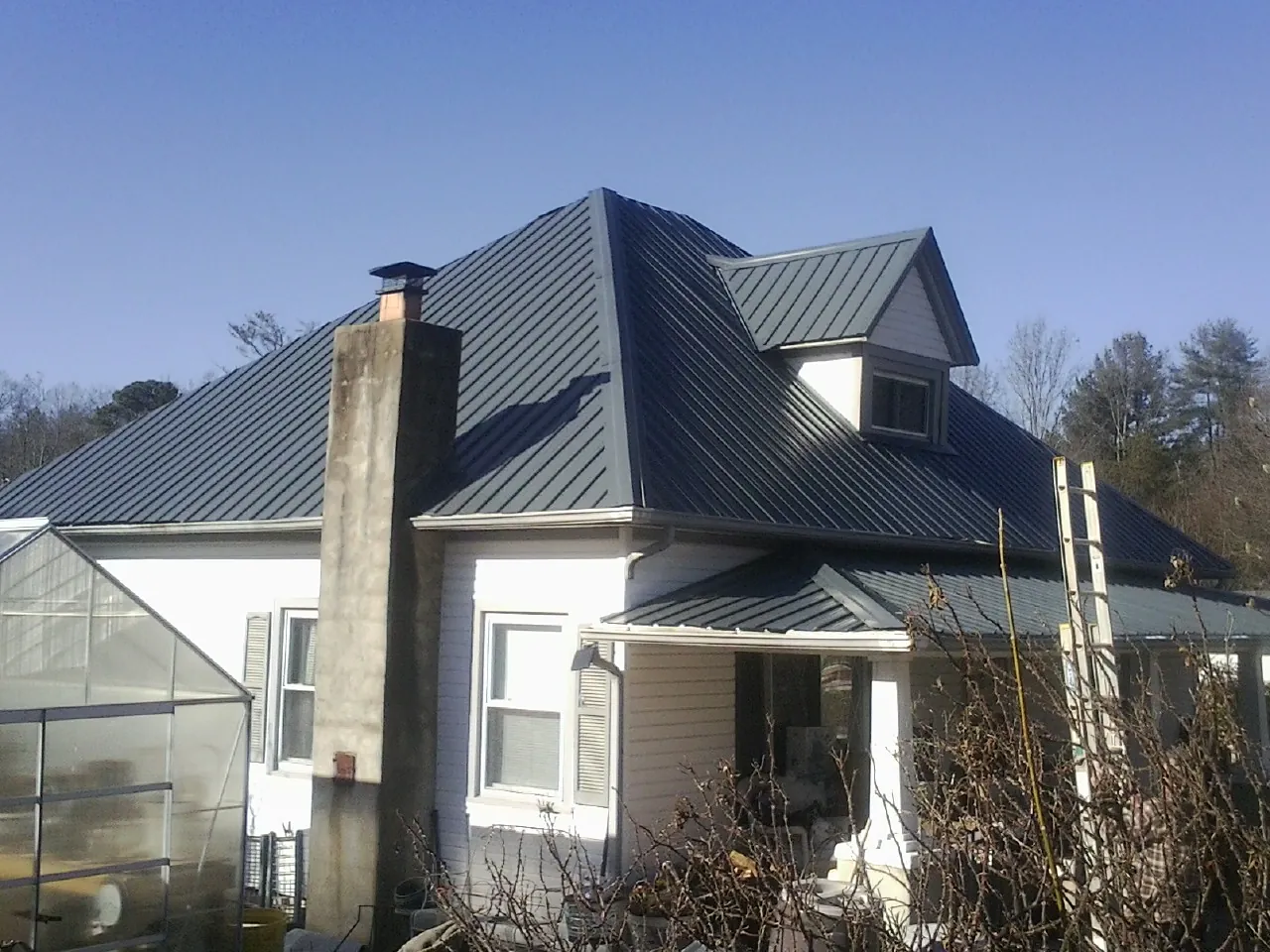 Dark blue standing seam metal roof on a white farmhouse with dormer — Slate & Tile Roof Repair by Roofing Brothers in Belspring