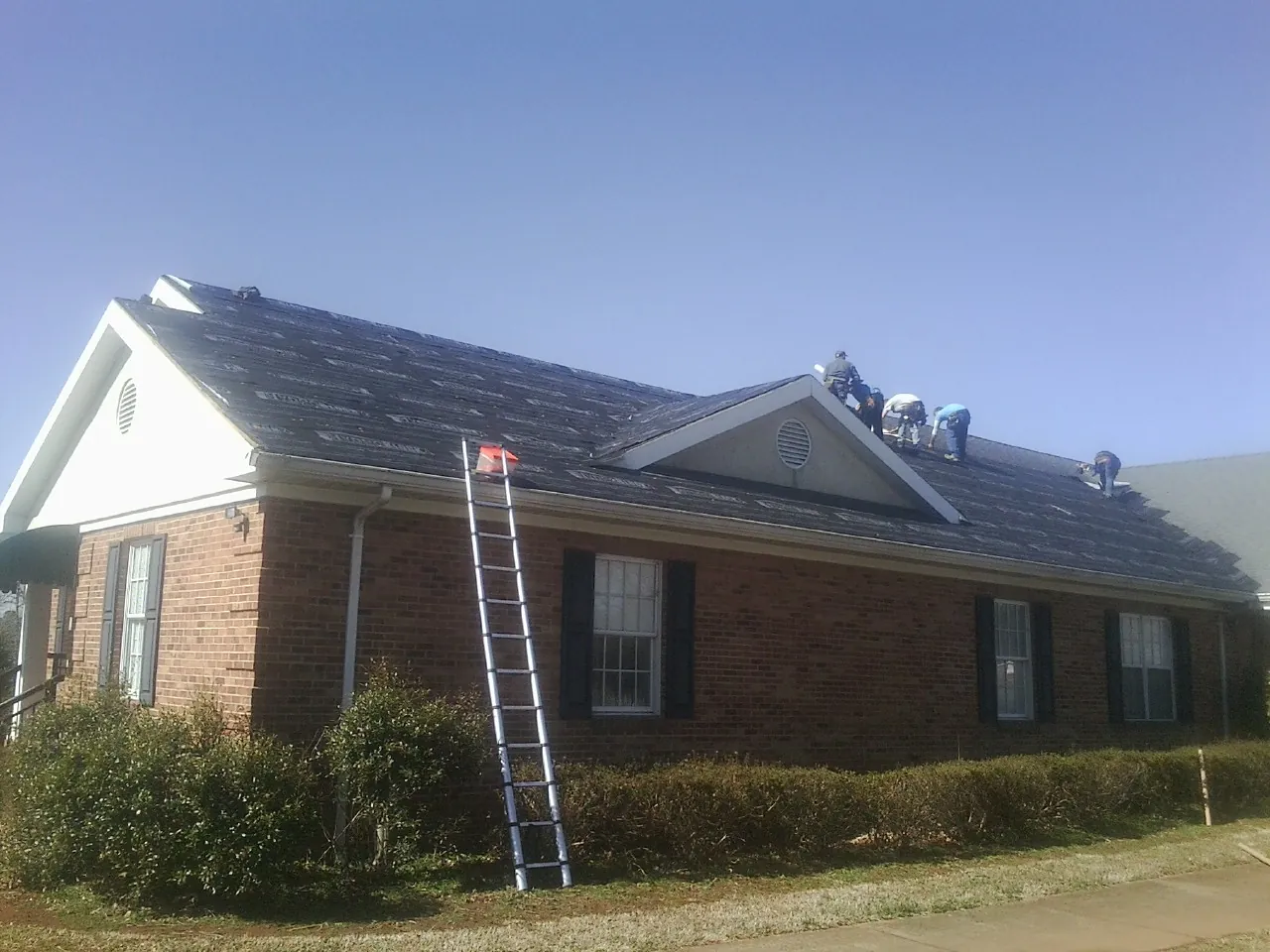Crew tearing shingles off a brick ranch roof with a ladder set — Metal Roof Repair work by our crew in Belspring