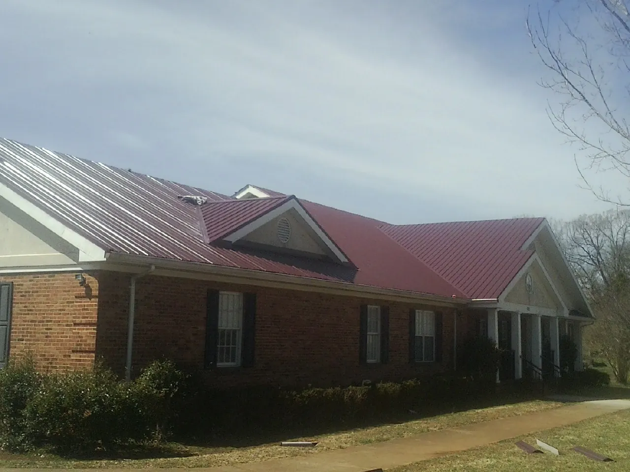 Red metal roof with gabled entries on a long brick building, from a Hail Damage Roof Repair job in Belspring