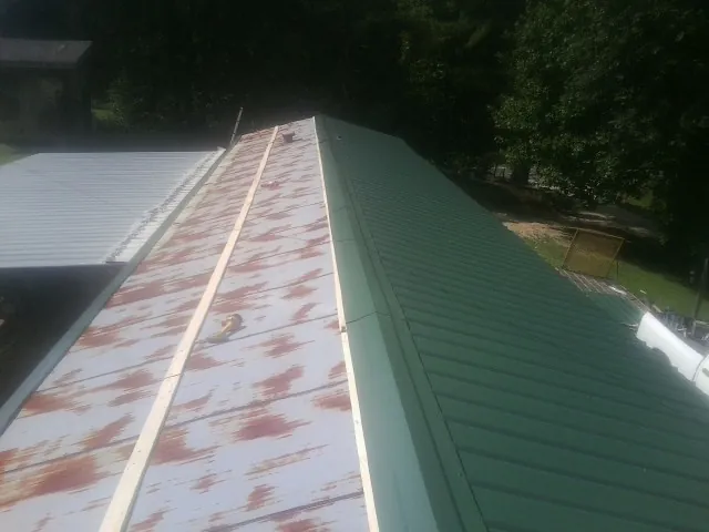 Old rusted panels beside newly installed green metal roofing — Wind Damage Roof Repair by Roofing Brothers in Belspring