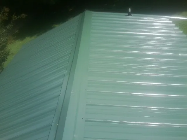 New green metal panels meeting at the ridge of a roof — Flat Roof Repair work by our crew in Belspring