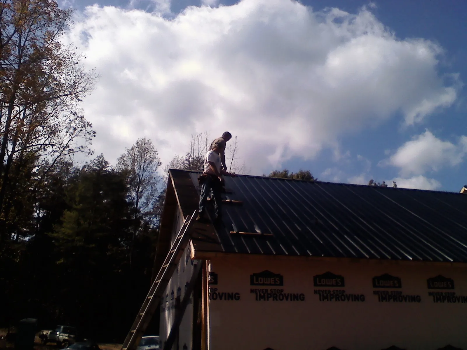 Roofer fastening dark metal panels high against a cloudy sky, from a Roof Inspection job in Belspring