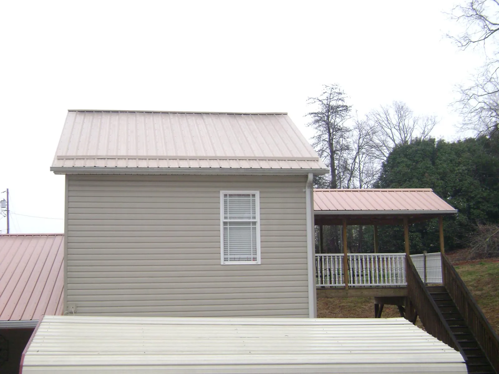 Tan metal roofs on a two story addition and attached porch, from a Roof Replacement job in Belspring